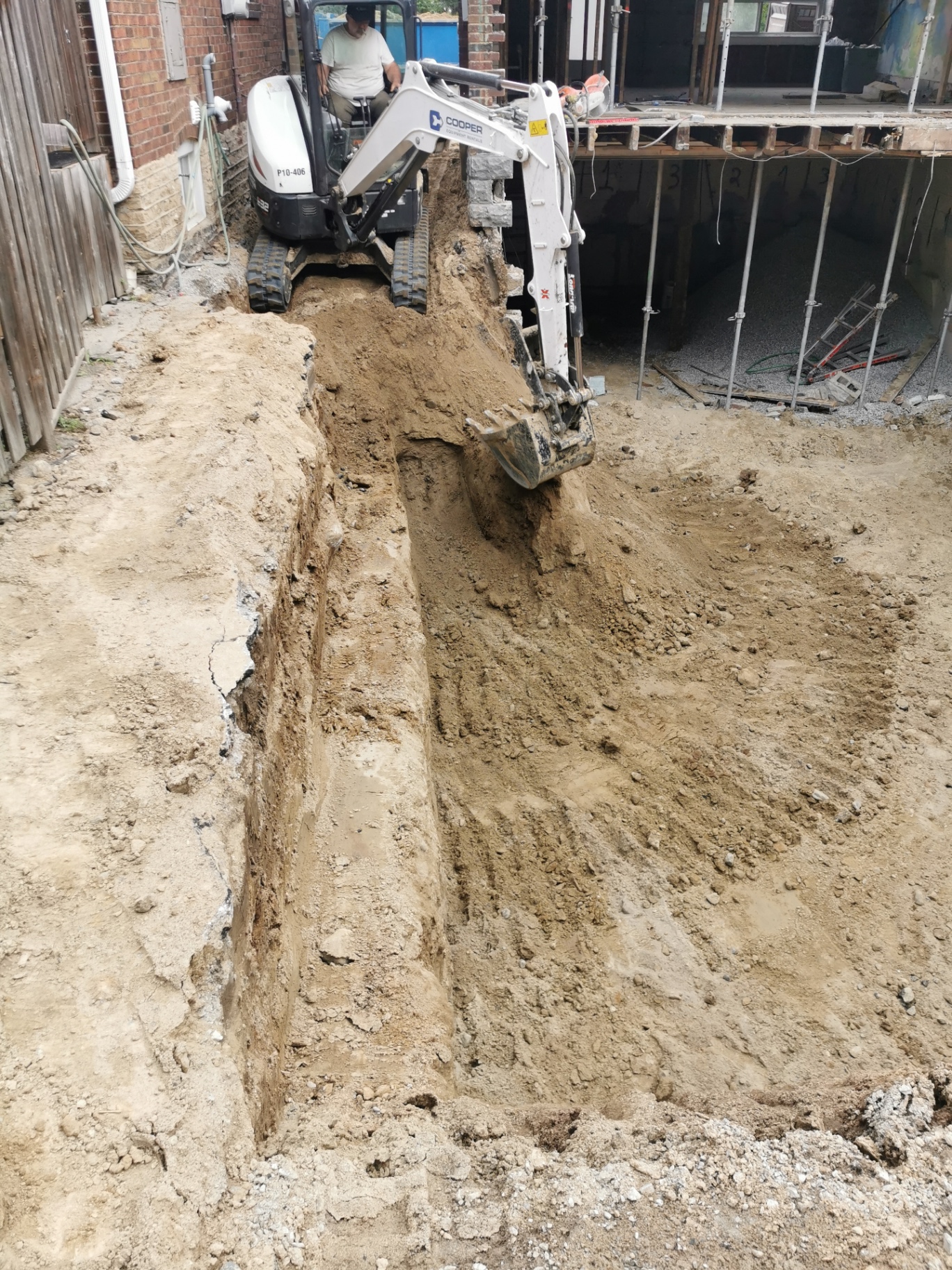Mini-excavator trenching alongside a foundation